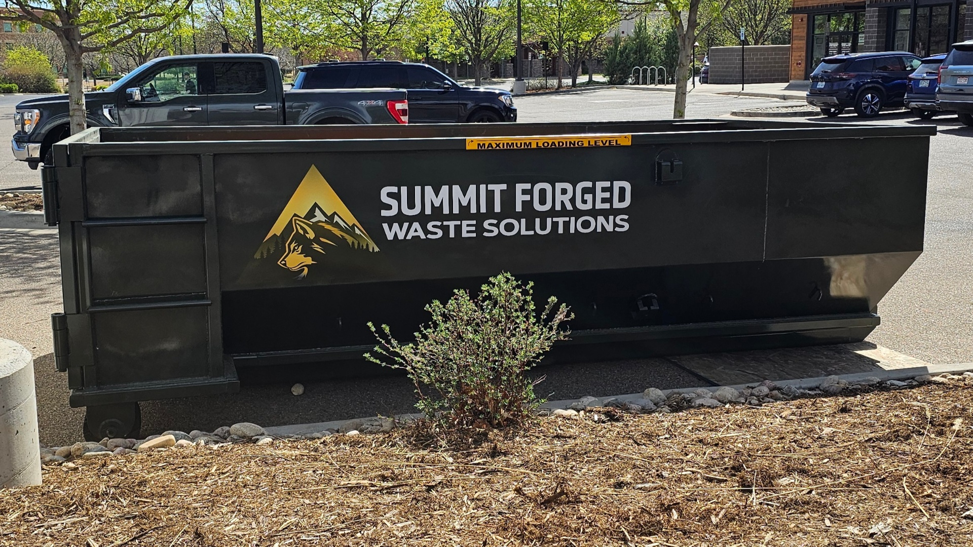 Summit Forged 10-yard roll-off dumpster delivered to a retail site in Northern Colorado, branded with the gold wolf and mountains logo